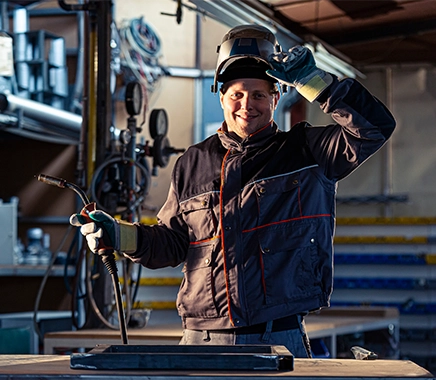 Glimlachende lasser die poseert op zijn werkplek in de fabriek, hij is aan het lassen